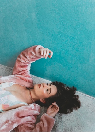 a person with a pink fur coat on laying on the carpet beside a turquoise wall