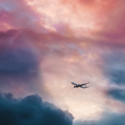 an airplane flying high in the sky featuring vibrant blue, red and pink clouds